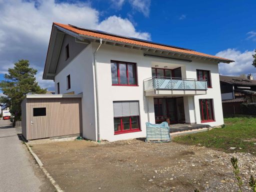 Modernes Haus mit Balkon, roter Fensterrahmung und angrenzender Garage.