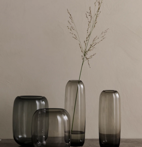 Schlichte, graue Glasvasen mit einem einzelnen Zweig in der höchsten Vase.