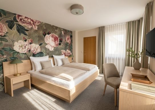 Helles Hotelzimmer mit Doppelbett, floralem Wandmuster und moderner Einrichtung.