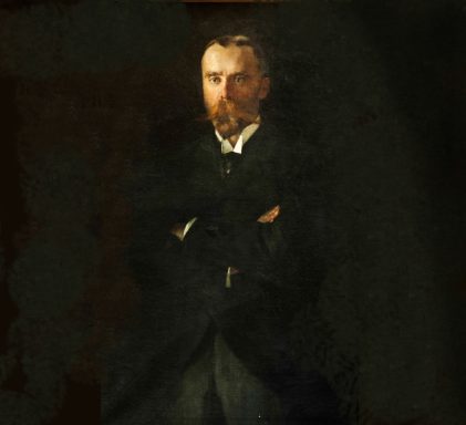 Porträt eines Mannes mit Bart, in dunkler Kleidung und verschränkten Armen.