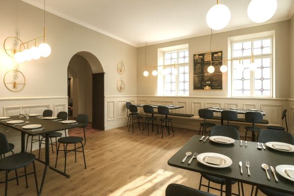 Heller Restaurantbereich mit Tischen, Stühlen und dekorativen Leuchten.