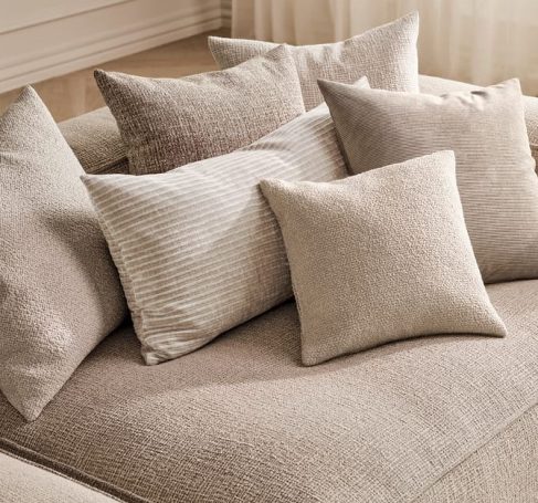 Verschiedene Kissen in neutralen Farbtönen auf einer Couch.