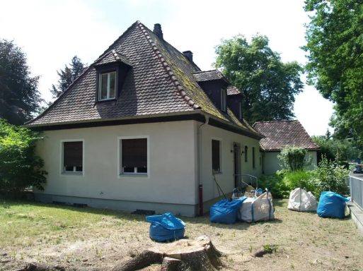 Ein einseitiges Haus mit braunem Dach, umgeben von Bäumen und verschiedenen Baustellenmaterialien.